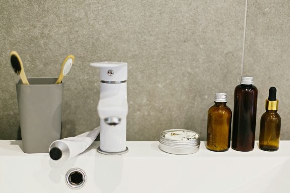 Toothbrushes, a dispenser, and various amber glass bottles on a bathroom countertop.